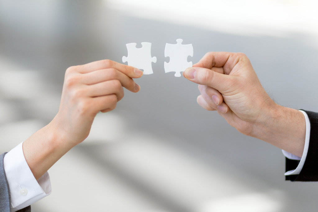 Hands of two business people each holding a puzzle piece side by side