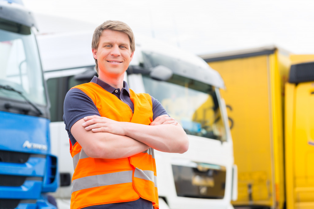 Logistics - proud driver or forwarder in front of trucks and trailers, on a transshipment point