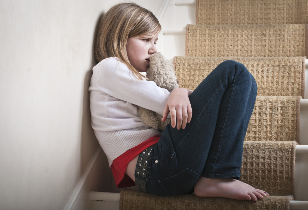 A lonely child, alone, sitting on a stair at home