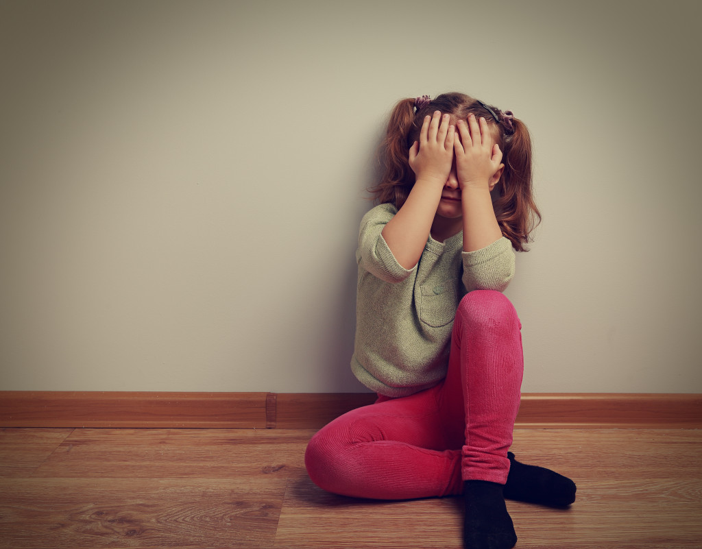 A scared and crying girl on the floor covering her face