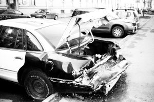 Grayscale Photo of Wrecked Car Parked Outside
