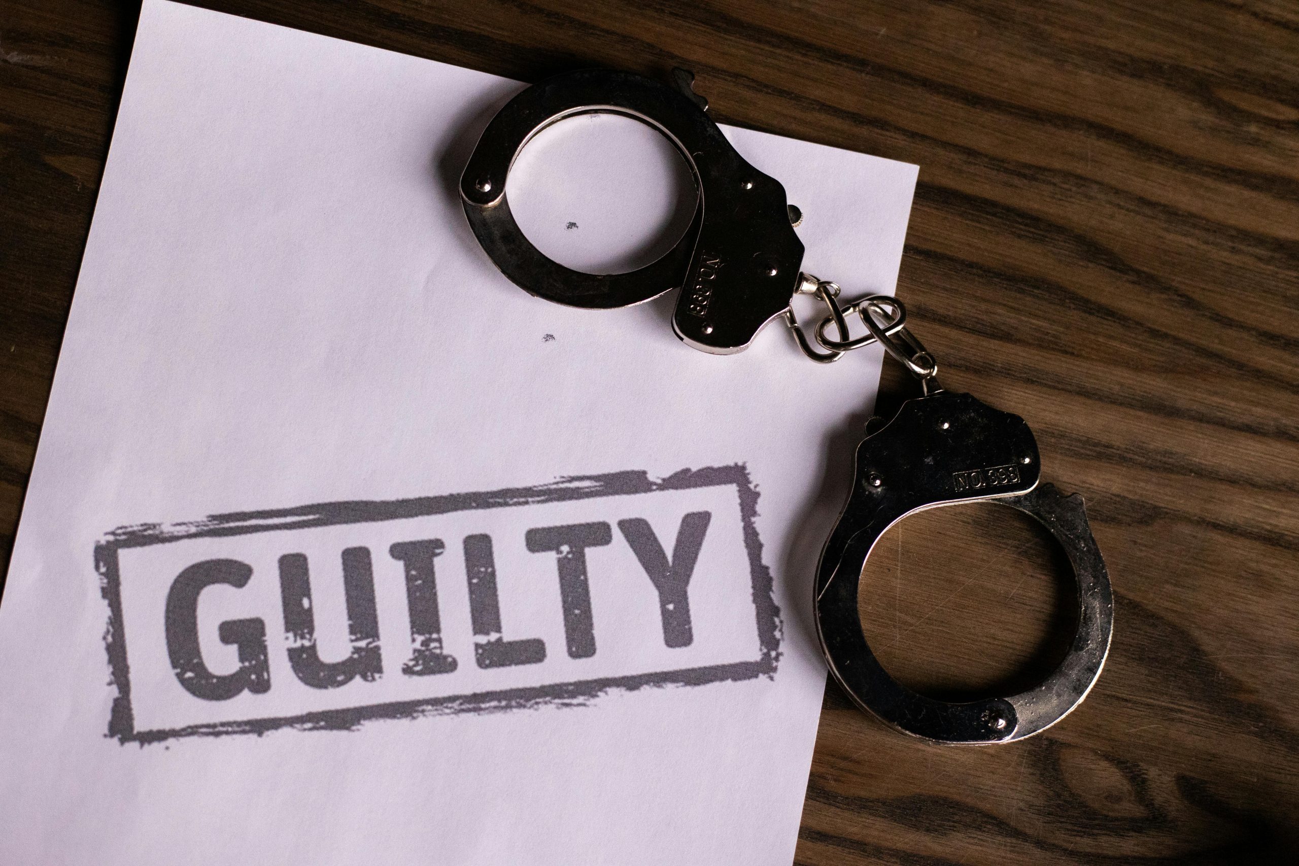 the word "guilty" printed on a sheet of paper next to a pair of handcuffs